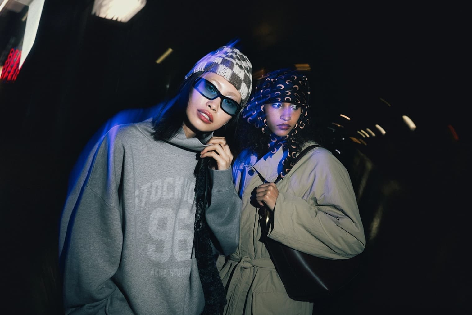Two women wearing Acne Studios sweat, Girls of Dust trench coat, F/CE tote bag and Peachy Den dress.