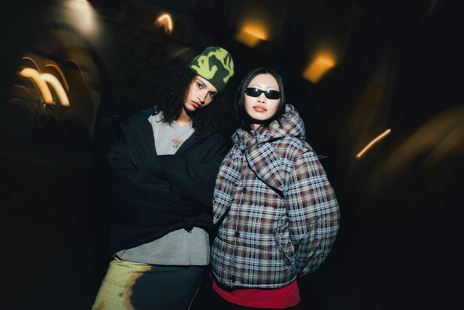 Two women stood wearing Sunday Fruit Market padded jacket, Ganni Mini Dress, and Damson Madder Rugby Shirt