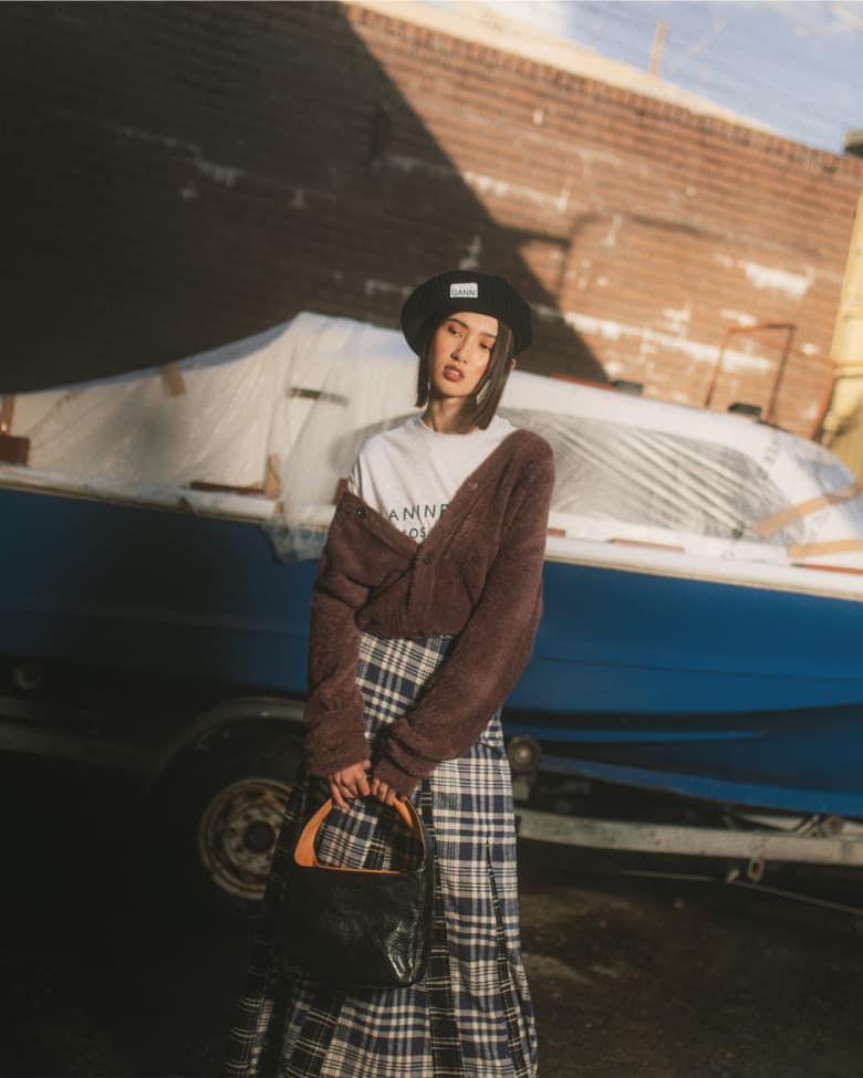 A woman stands in front of a boat wearing a plaid skirt and a beret. 