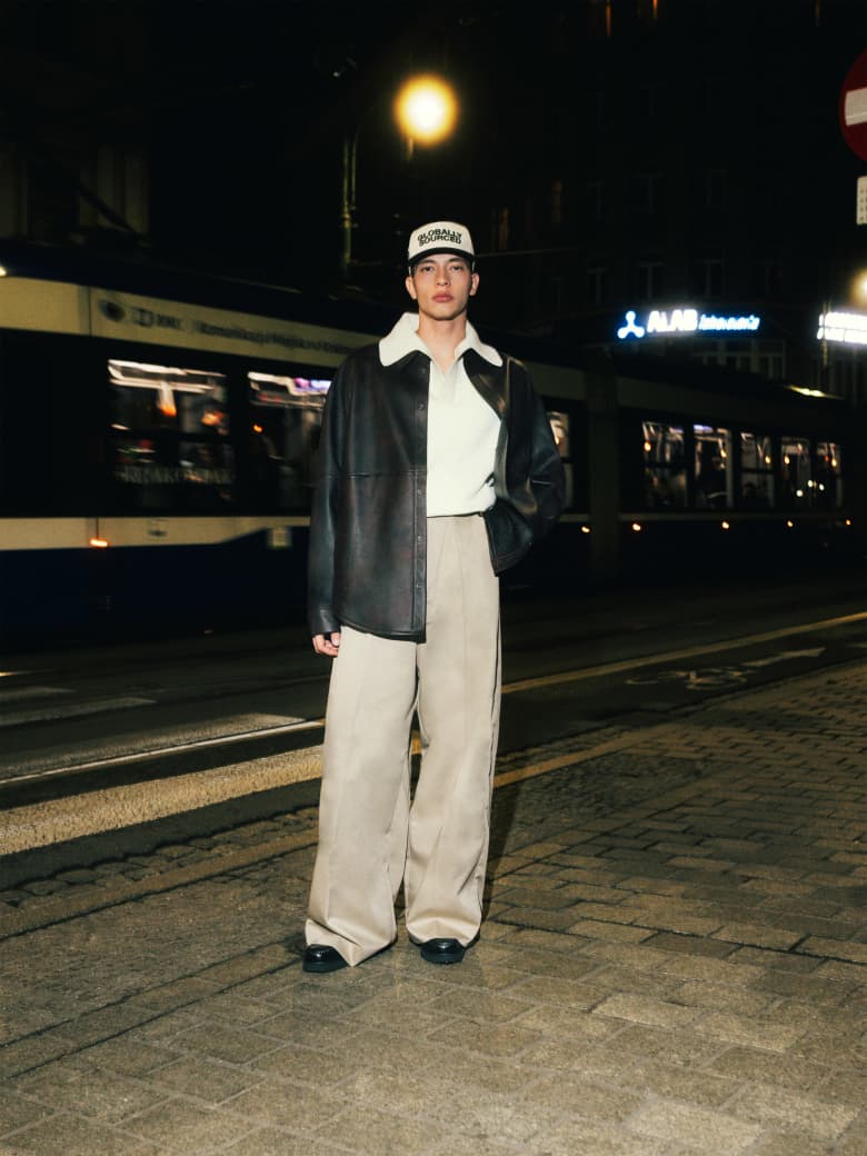 A man wearing Acne Studios leather shirt, Jacquemus jumper, Willy Chavarria trousers and Bass Weejun loafers. 