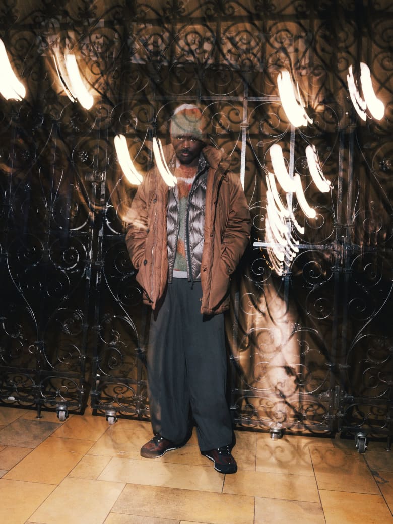 A man wearing a Ranra coat, This Is Never That vest, Merely Made trousers and Asics sneakers.