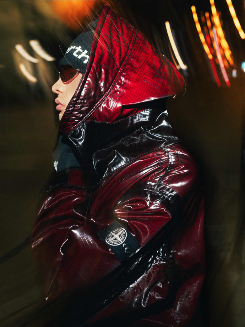 A man wearing a red Stone Island coat, Loewe sunglasses, This Is Never That beanie and The North Face gloves. 