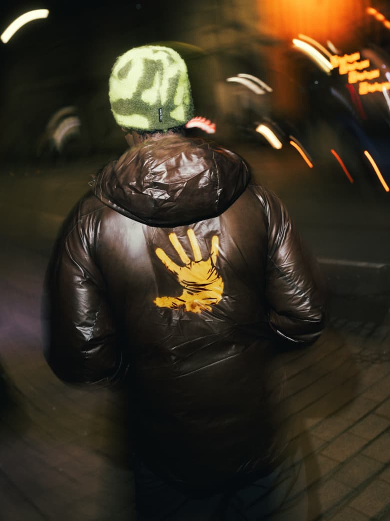 A man wearing Purple Mountain Observatory coat, with a hand print on it to show the heat colour changing technology.