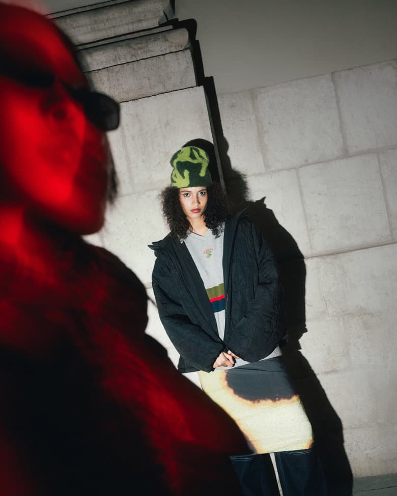 Woman stood wearing Gramicci beanie, Sunday Fruit Market padded jacket and Feners skirt.