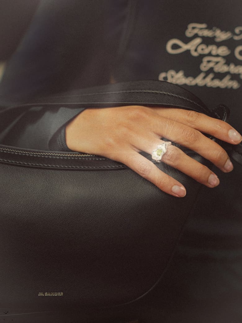 "Woman wearing a Simuero Ola Ring in  Silver & Green Peridot holding a Jil Sander Knot Cross Body Bag."