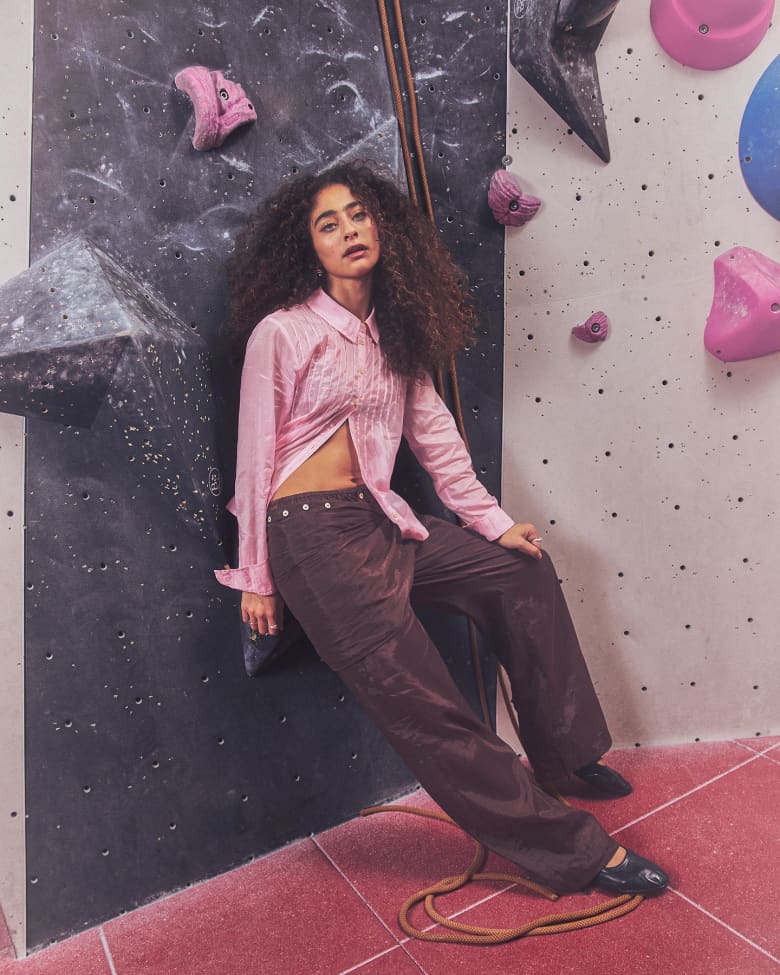 Deba Hekmat wearing a pink Damson Madder Presented by END. Shirt leaning against a wall