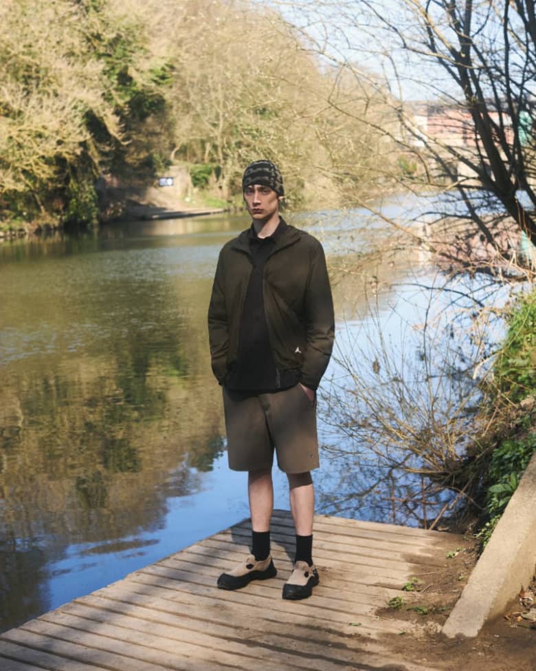 A man stands by a lake in a lightweight technical jacket