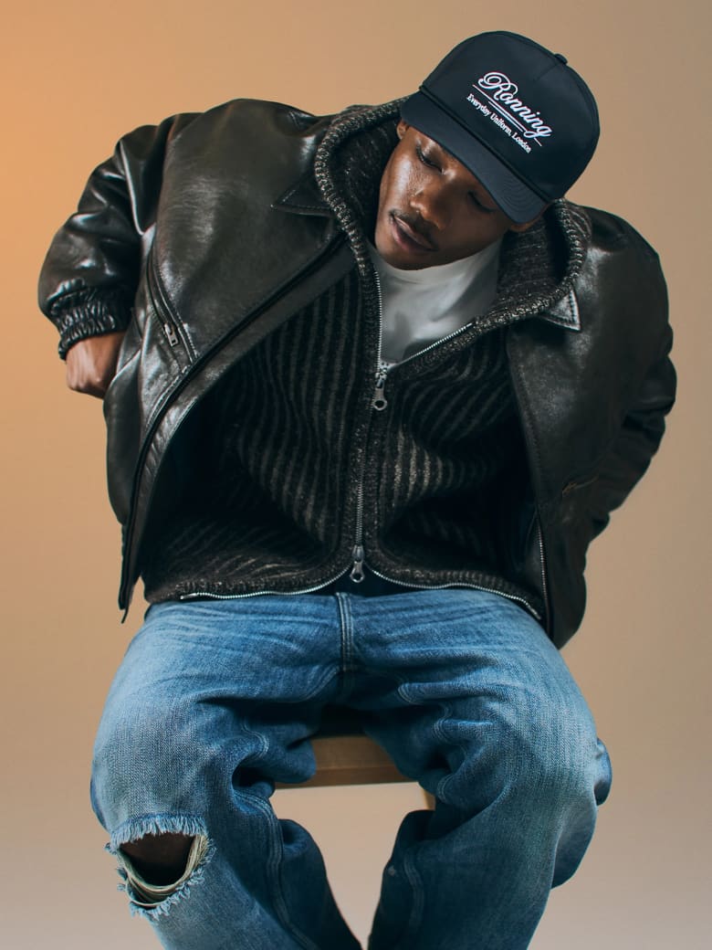 A man sitting wearing a black leather jacket and blue jeans. 