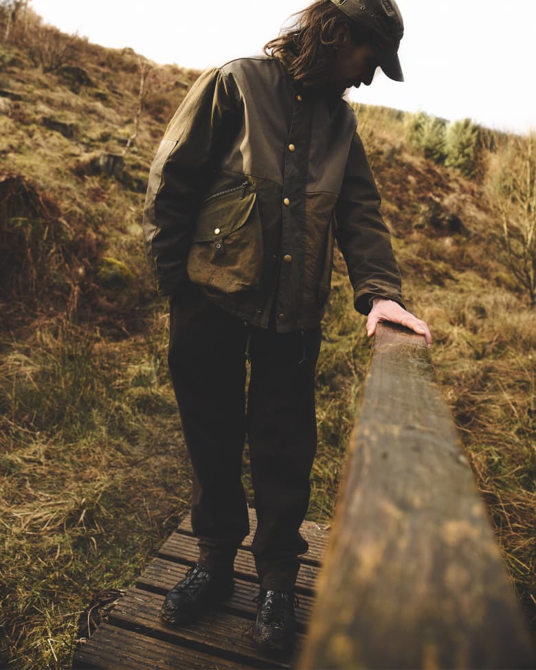 A man standing outside in the countryside holding onto a wooden railing. 