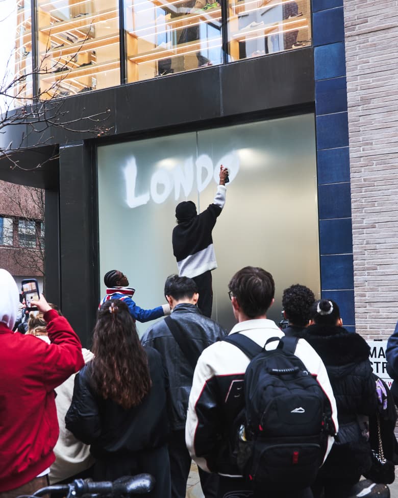 A man spray paints the word "London" in white paint on a shop window. 