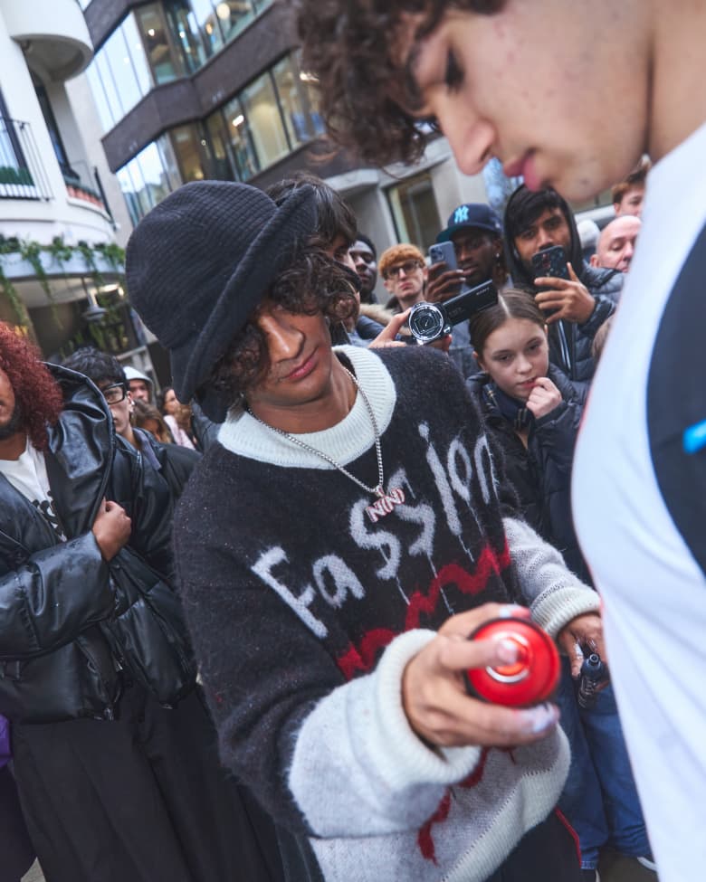A man spray paints another man's white t-shirt with red paint. 