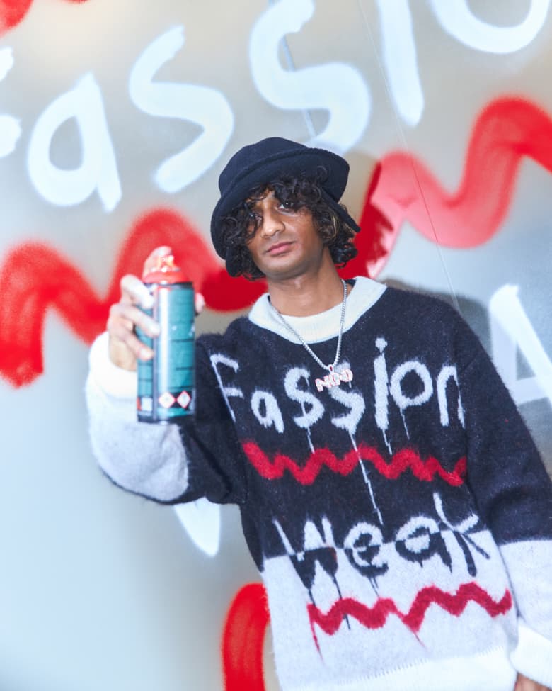 Artist Navinder Nangla poses in front of a spray painted window holding up a can of spray paint. 