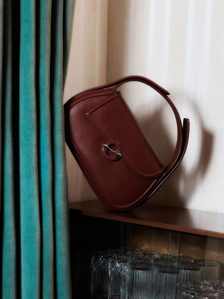 A burgundy leather handbag stands on its side next to a turquoise curtain. 