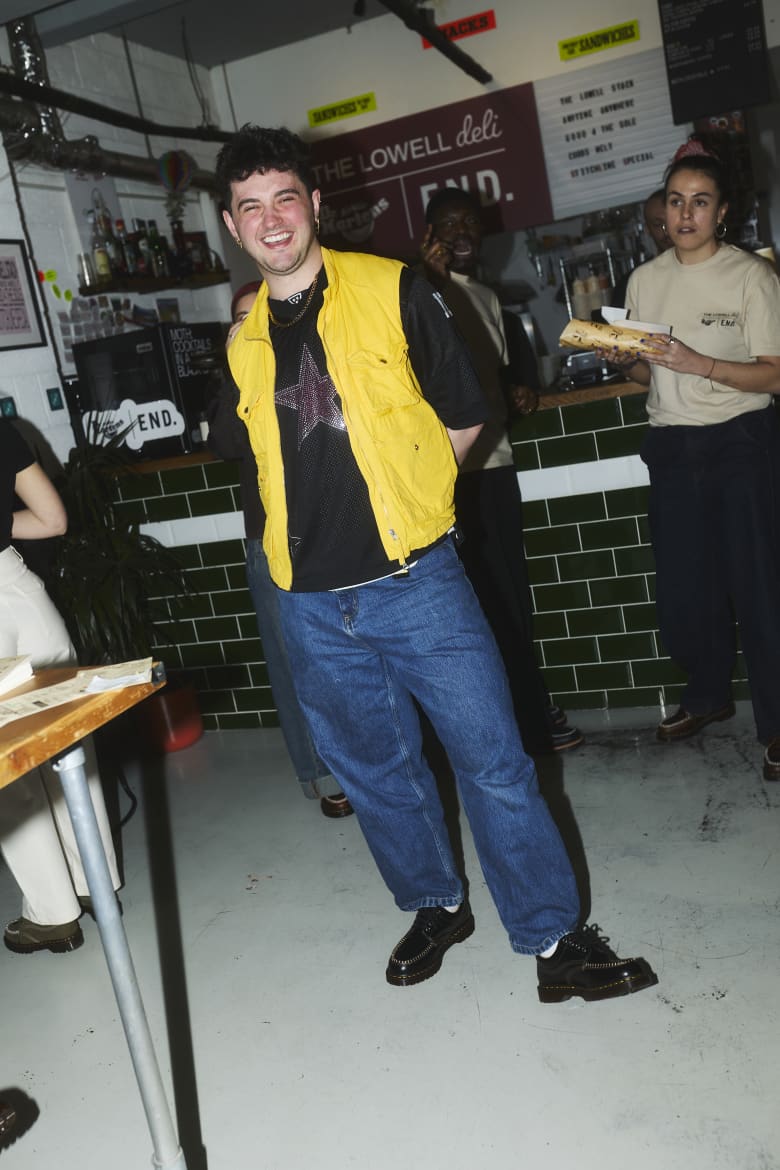 A man wearing a yellow gilet vest standing in the middle of a shop. 
